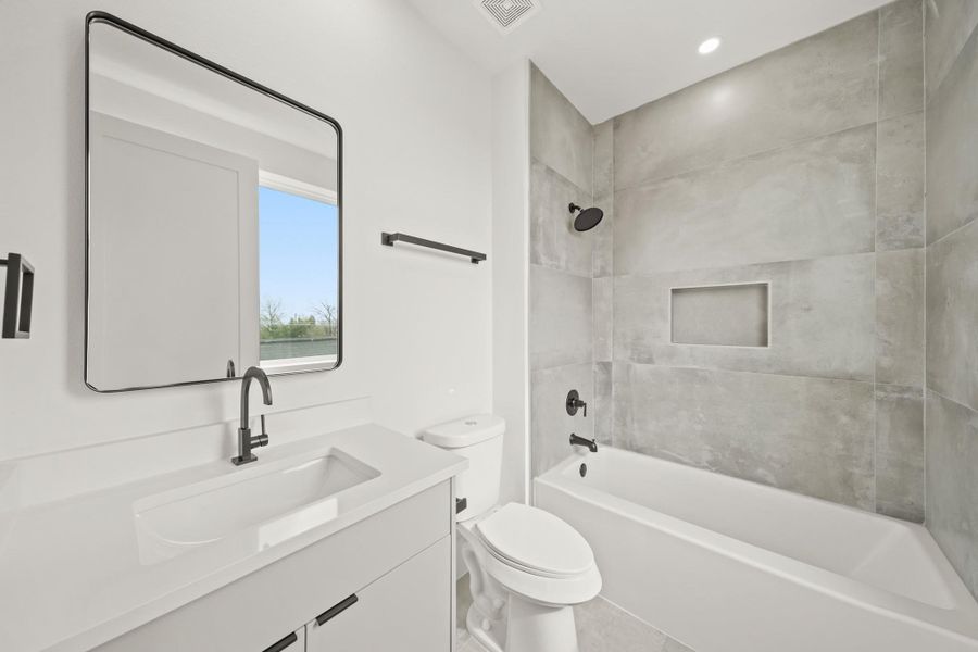 Bright and cheery, the second private bath includes a Quartz counter with an under mount sink and a black framed mirror. The tub/shower combination has tile surrounded walls and floors, as well as a built-in niche for soap and shampoo.