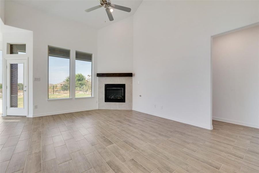 Unfurnished living room featuring a tile fireplace, a high ceiling, light wood-type flooring, and ceiling fan