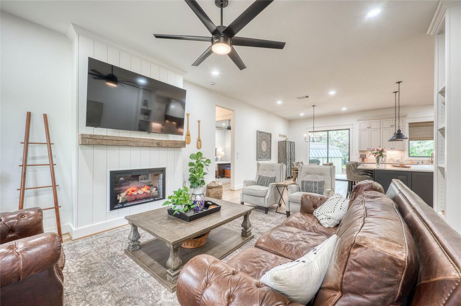 Living area featuring a shiplap-accented fireplace with a wood mantle, recessed lighting, and a ceiling fan