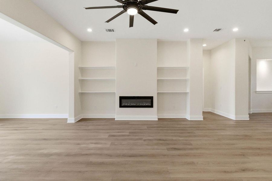A well-lit living space features built-in shelving, an electric fireplace, and durable wood-look flooring. A well-lit living space features built-in shelving, an electric fireplace, and durable wood-look flooring.