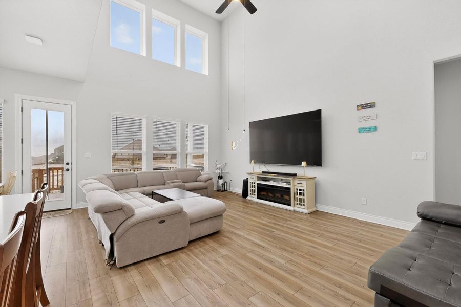 Living area featuring light wood-style flooring, ceiling fan, a towering ceiling, and a fireplace