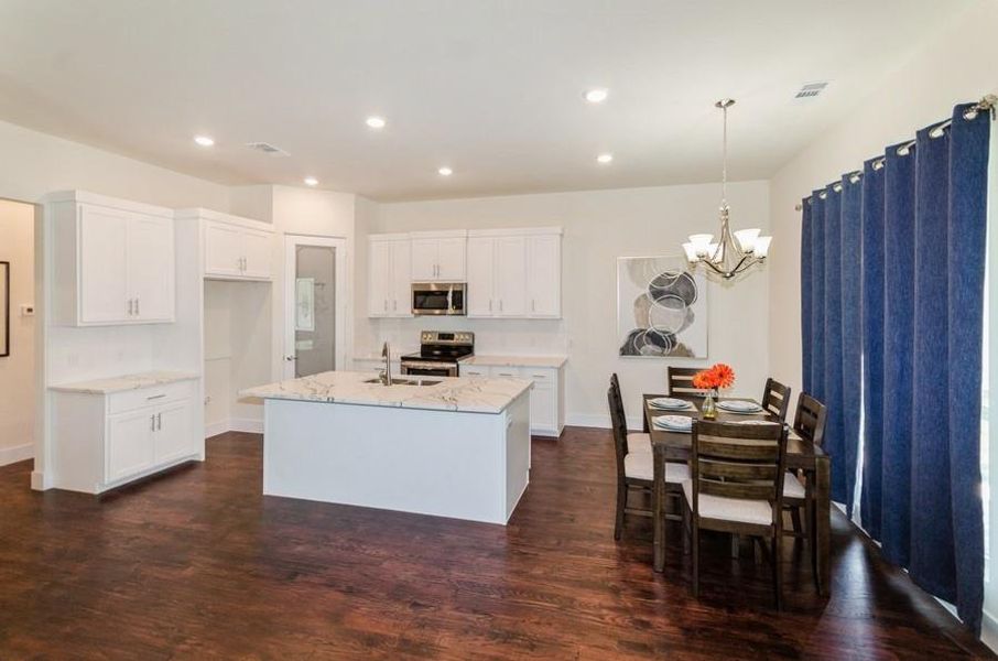 Kitchen featuring a center island with sink, appliances with stainless steel finishes, dark wood-type flooring, hanging light fixtures, and white cabinets