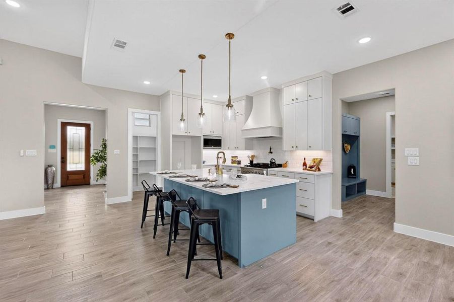 Kitchen with custom exhaust hood, a center island with sink, a kitchen breakfast bar, pendant lighting, and white cabinets