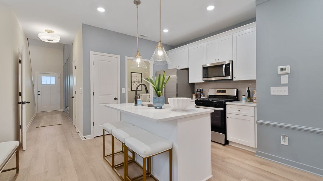 Bright open kitchen featuring center island, white cabinets, quartz counters, and stainless steel range and microwave.