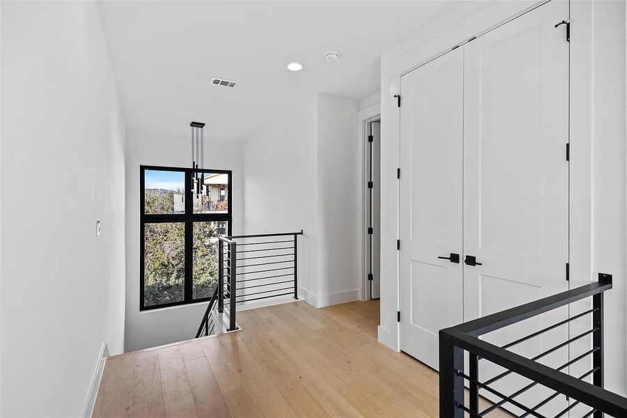Upper landing with warm hardwood flooring and modern stair railing.