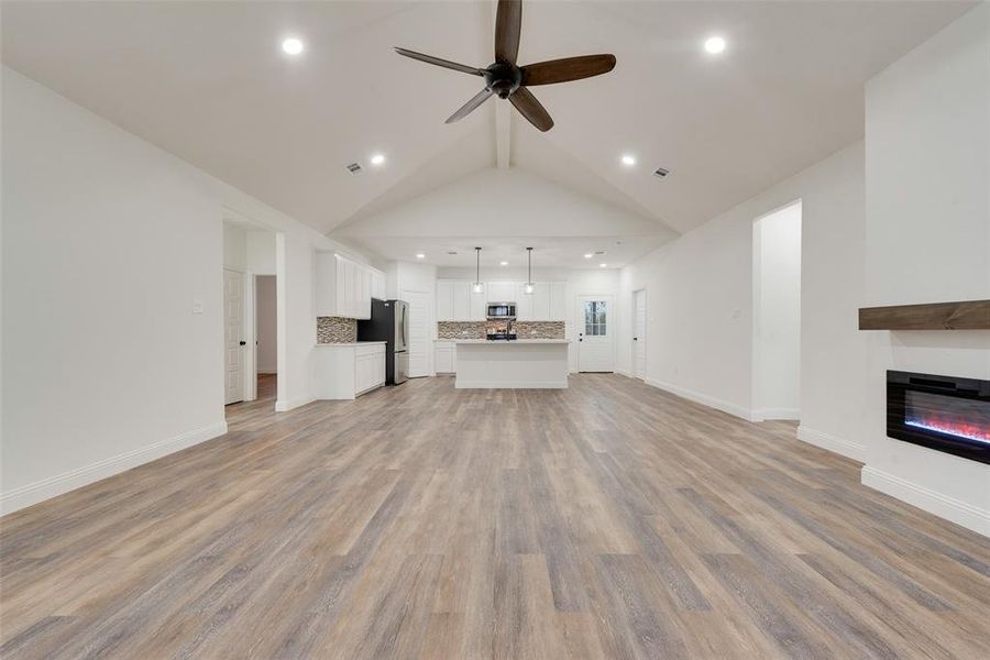 Unfurnished living room featuring light hardwood / wood-style flooring, lofted ceiling, and ceiling fan