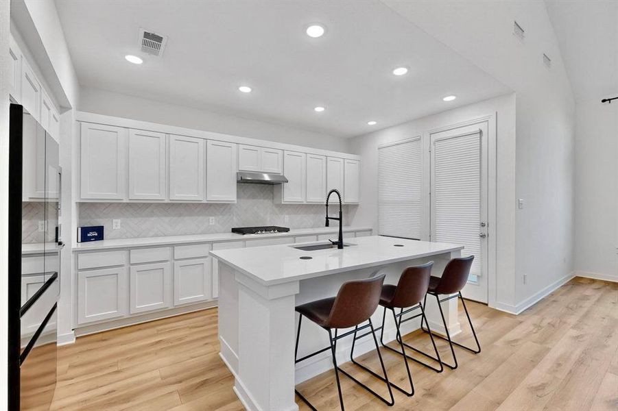 Kitchen featuring decorative backsplash, a kitchen island with sink, white cabinets, a kitchen breakfast bar, and recessed lighting Kitchen featuring decorative backsplash, a kitchen island with sink, white cabinets, a kitchen breakfast bar, and recessed lighting