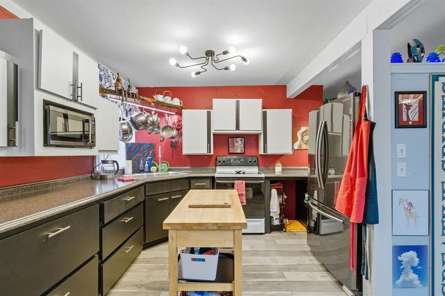 Kitchen with white cabinetry, stainless steel appliances, light wood-style floors, dark countertops, and beam ceiling Kitchen with white cabinetry, stainless steel appliances, light wood-style floors, dark countertops, and beam ceiling