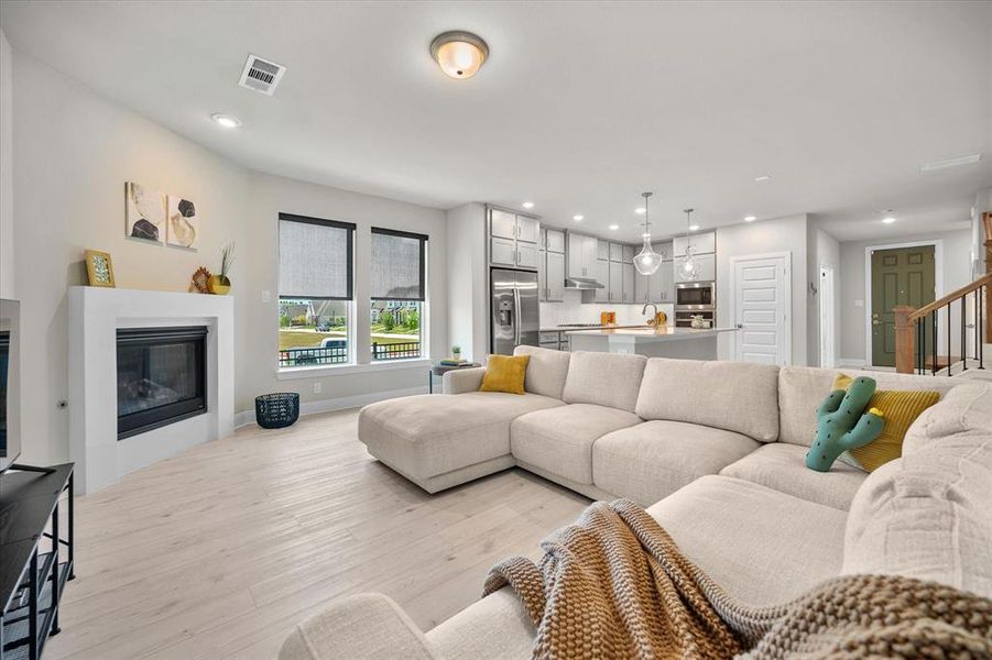 Living room with light wood finished floors, recessed lighting, and a glass covered fireplace Living room with light wood finished floors, recessed lighting, and a glass covered fireplace