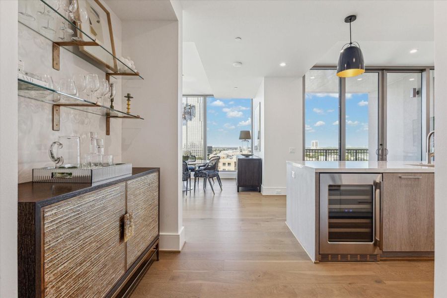 Entry corridor with glass shelving and an option for a built-in bar, flowing into the open dining and living space framed by large windows and abundant natural light. Photos are of a similar unit with the same floor plan