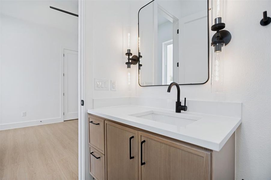Bathroom vanity featuring a light wood-finish base, integrated white sink, matte black faucet, and rectangular mirror