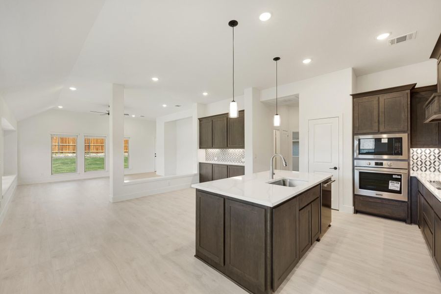 Open kitchen with dark wood cabinets, large island, white countertops, and stainless steel appliances, open to living area.