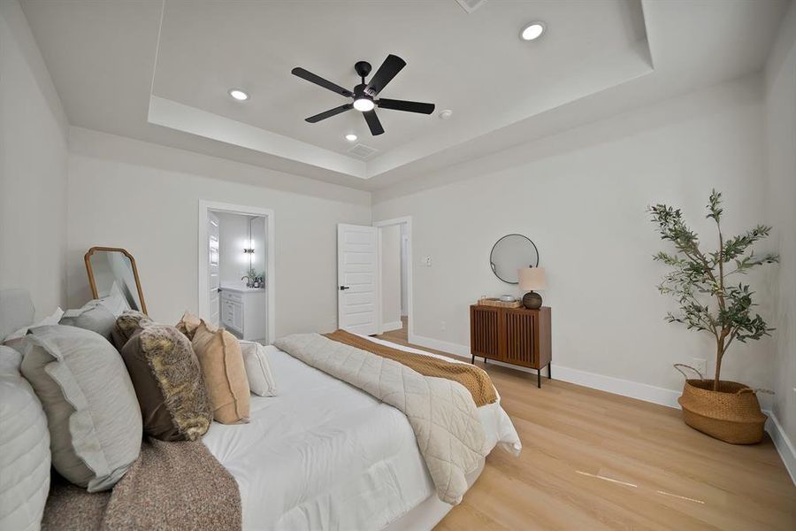 Bedroom with a tray ceiling, wood finished floors, recessed lighting, ensuite bathroom, and ceiling fan Bedroom with a tray ceiling, wood finished floors, recessed lighting, ensuite bathroom, and ceiling fan