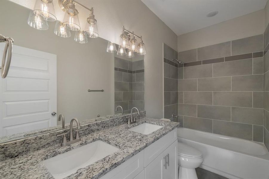 Full bathroom featuring double vanity, tiled shower / bath combo, and toilet