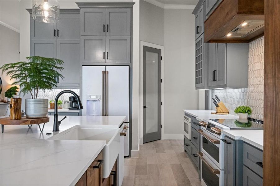 Kitchen featuring premium appliances, crown molding, premium range hood, pantry and light stone counters