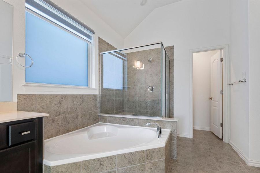Bathroom featuring a stall shower, a garden tub, vanity, and vaulted ceiling Bathroom featuring a stall shower, a garden tub, vanity, and vaulted ceiling