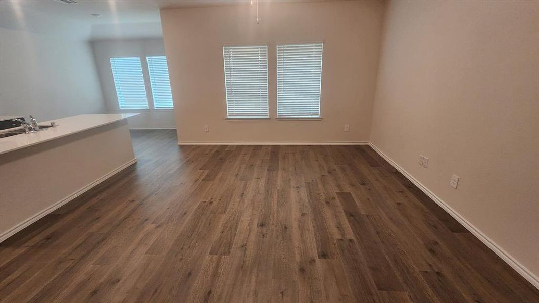 Open concept living space featuring wood-finish flooring, neutral wall tones, and multiple windows with blinds Open concept living space featuring wood-finish flooring, neutral wall tones, and multiple windows with blinds
