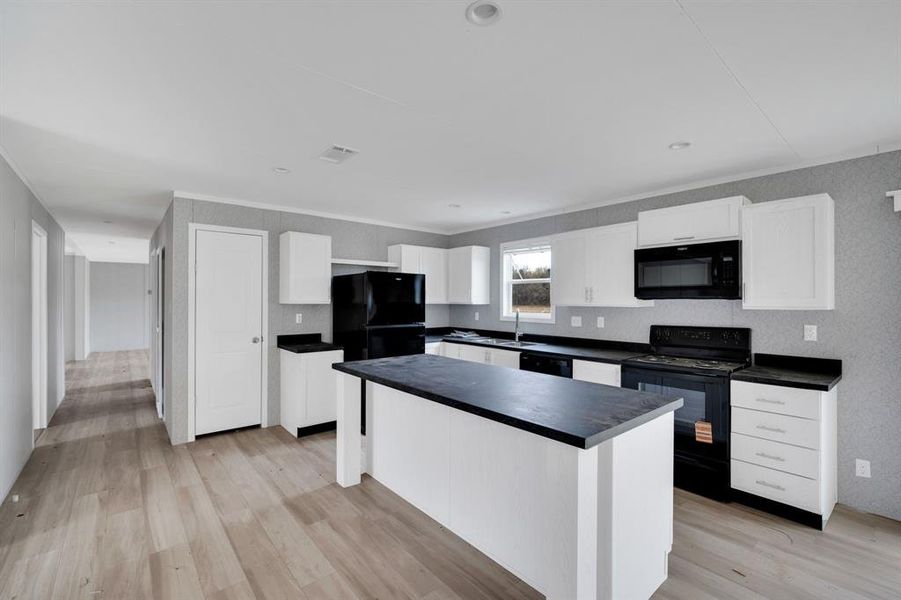 Kitchen with black appliances, white cabinetry, light wood finished floors, dark countertops, and a center island