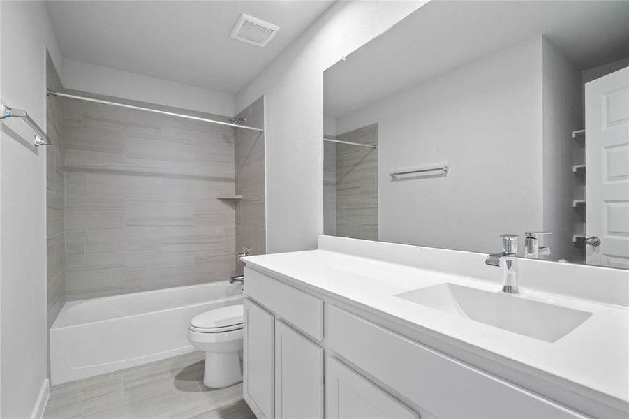 Secondary bath features tile flooring, bath/shower combo with tile surround, stained wood cabinets, beautiful light countertops, mirror, sleek fixtures and modern finishes!