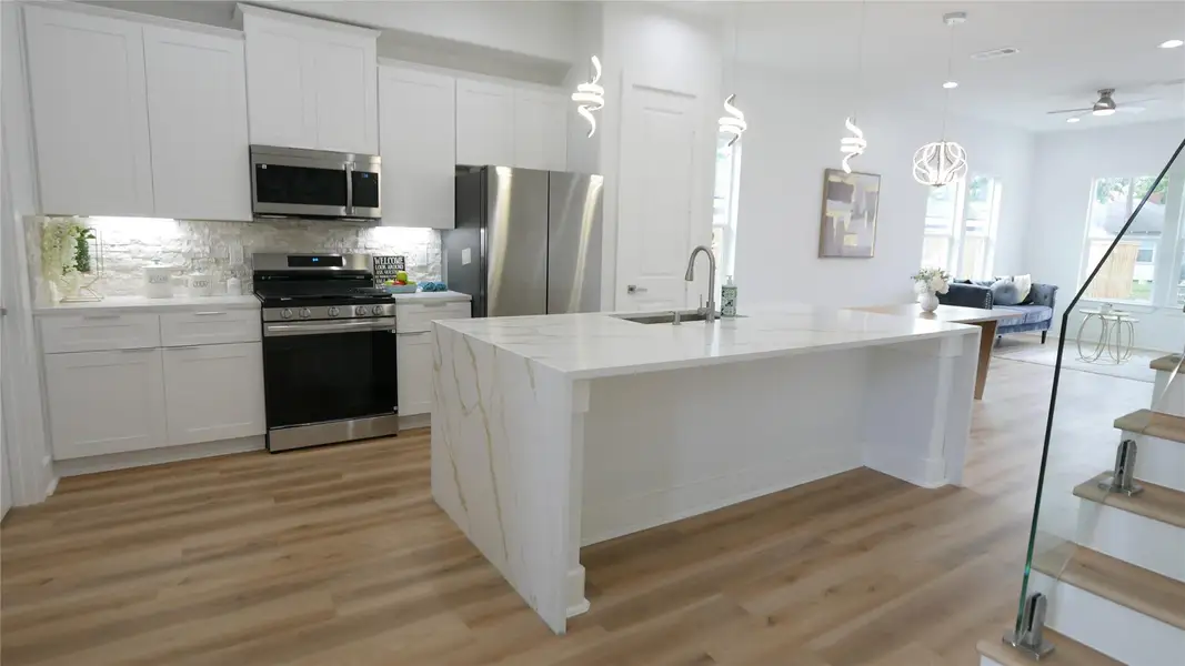 This modern kitchen features sleek white cabinetry, stainless steel appliances, and a large luxury island with a built-in sink. The open layout connects to a bright living area, emphasizing natural light and contemporary design. This modern kitchen features sleek white cabinetry, stainless steel appliances, and a large luxury island with a built-in sink. The open layout connects to a bright living area, emphasizing natural light and contemporary design.