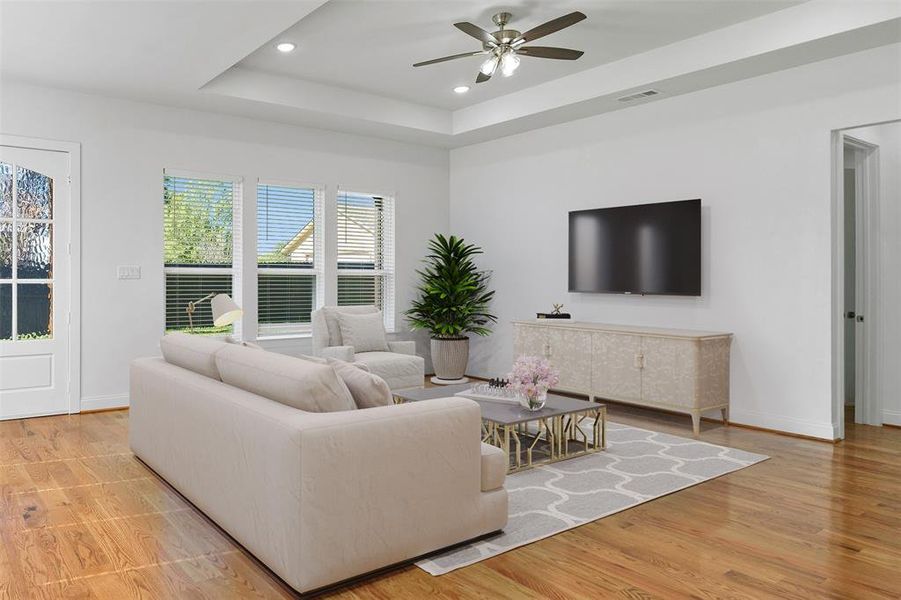 Living room featuring light wood-type flooring, ceiling fan, and a tray ceiling