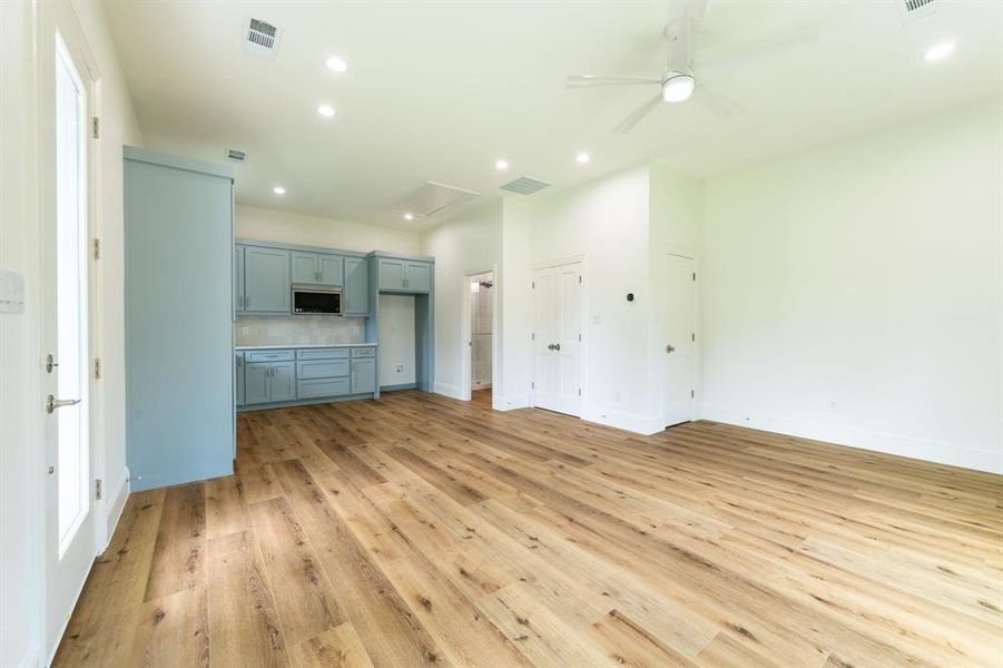 Open-concept space featuring wood-finish flooring, a contemporary ceiling fan, recessed lighting, light blue cabinetry with an integrated microwave, and white walls Open-concept space featuring wood-finish flooring, a contemporary ceiling fan, recessed lighting, light blue cabinetry with an integrated microwave, and white walls