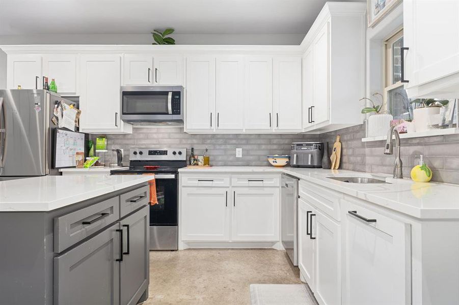 Kitchen with sink, appliances with stainless steel finishes, white cabinetry, gray cabinetry, and light stone countertops