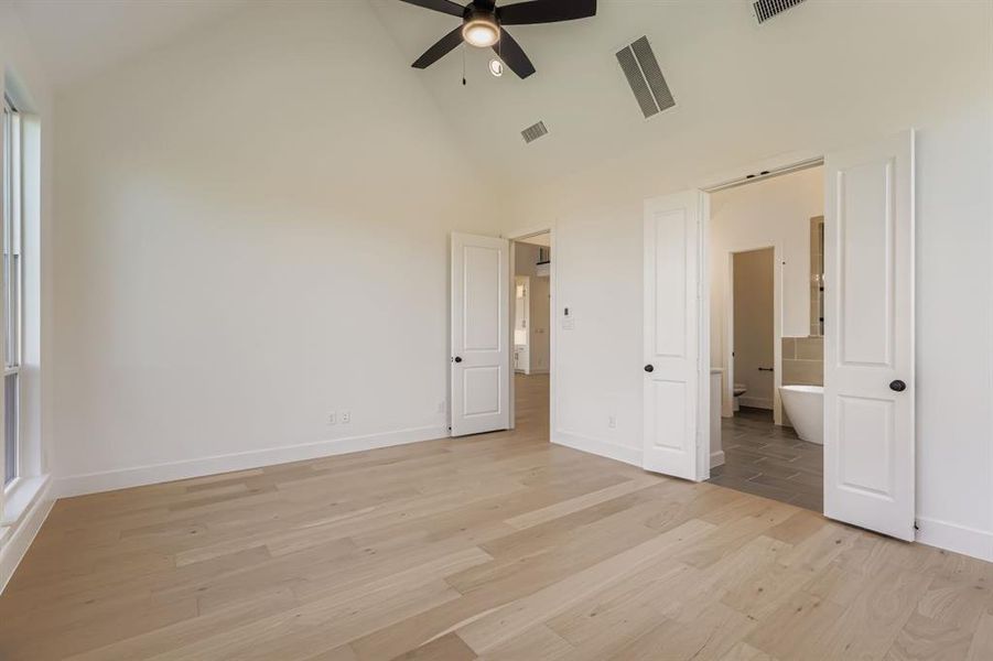 Unfurnished bedroom with light wood-type flooring, high vaulted ceiling, a ceiling fan, and ensuite bath