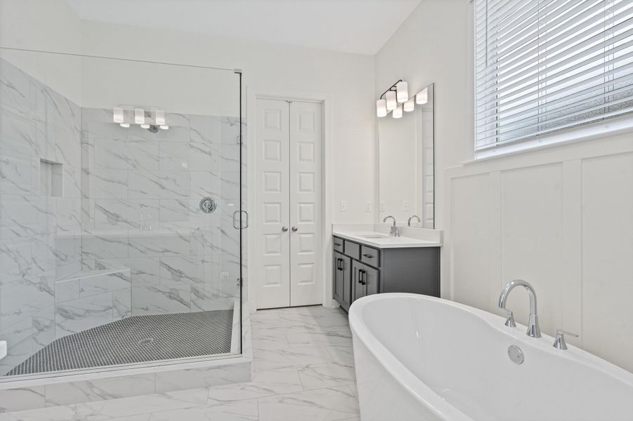Spacious bathroom featuring a frameless glass shower with marble-look tile, a built-in shower bench, and a dual vanity with a quartz countertop