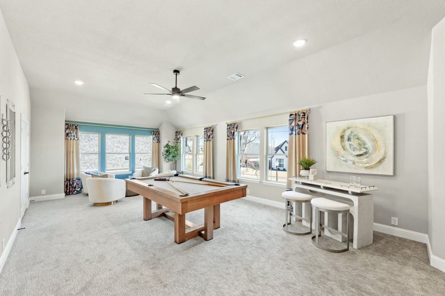 Game room with wood pool table, vaulted ceiling, ceiling fan, and large windows with carpet flooring Game room with wood pool table, vaulted ceiling, ceiling fan, and large windows with carpet flooring