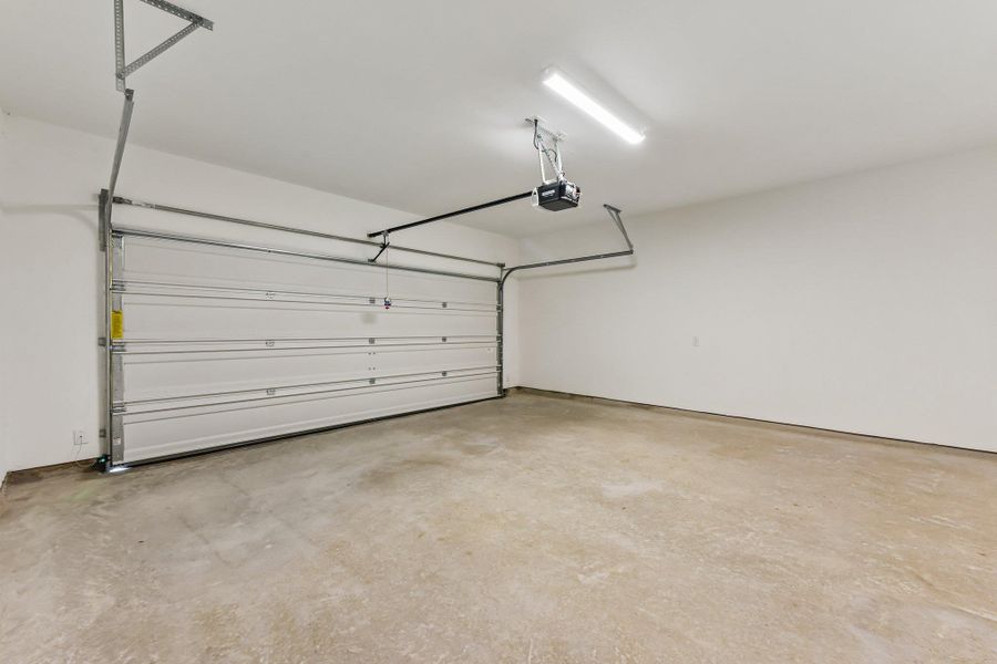 Spacious garage featuring a concrete floor, white walls, and a sectional garage door with an automatic opener