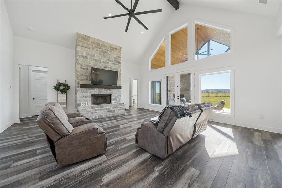 Living area with a stone fireplace, high vaulted ceiling, a ceiling fan, dark wood-type flooring, and beamed ceiling