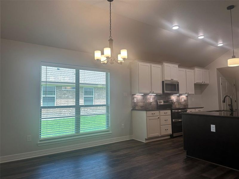 Kitchen featuring stainless steel appliances, dark countertops, lofted ceiling, backsplash, and a chandelier