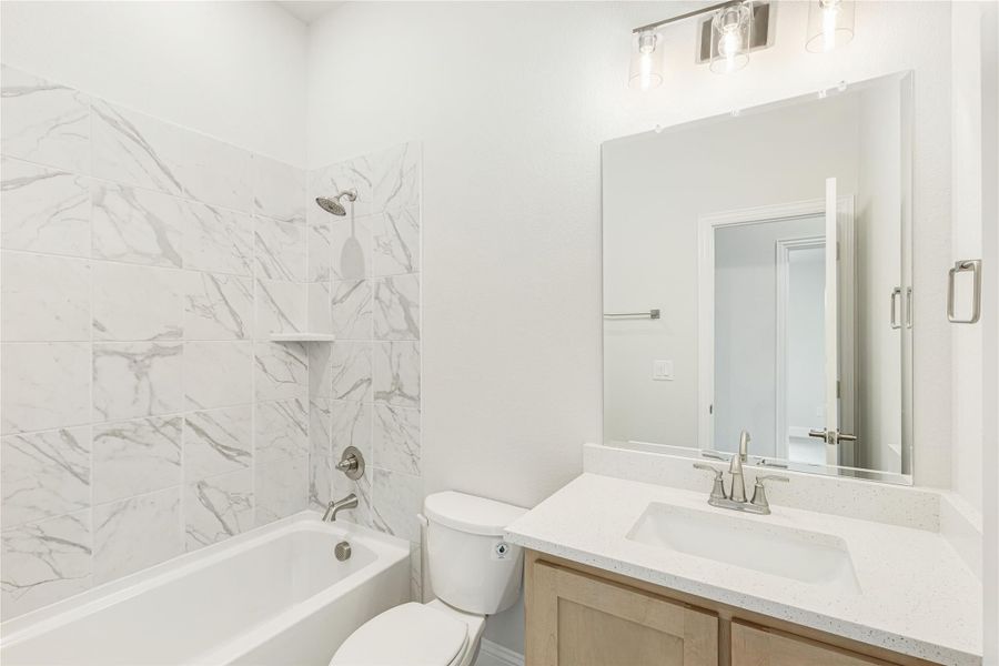 Bathroom with marble-tile tub and shower, single vanity with quartz countertop, and modern light fixture. Bathroom with marble-tile tub and shower, single vanity with quartz countertop, and modern light fixture.