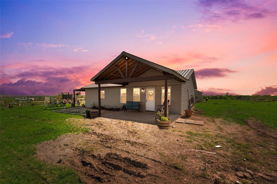 Back of house at dusk with a patio, a yard, and metal roof