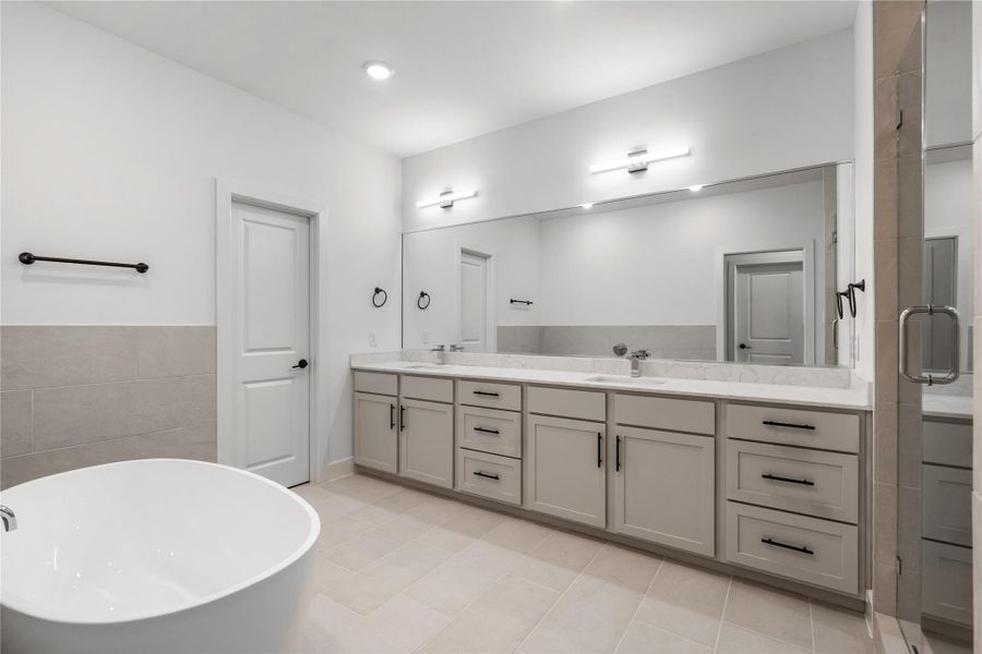 Spa-inspired primary bathroom — standalone soaking tub, quartz double vanity with extended mirror, LED vanity lighting bars, and frameless glass shower enclosure.