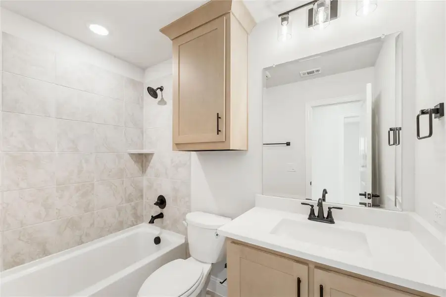 Bathroom with tiled tub-shower combo, light wood vanity, white countertop, and large mirror with pendant lights
