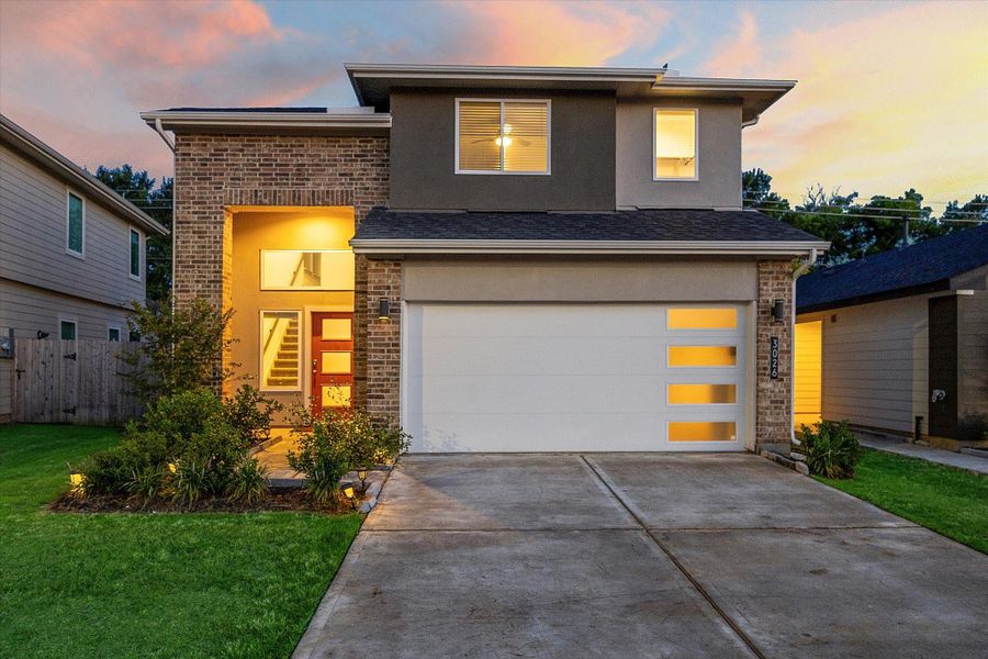 At golden hour, this home shines with its bold modern profile, brick-accented exterior, and oversized windows. A wide driveway, illuminated walkway, and fresh landscaping enhance the curb appeal while the full-lite red front door adds personality and charm. At golden hour, this home shines with its bold modern profile, brick-accented exterior, and oversized windows. A wide driveway, illuminated walkway, and fresh landscaping enhance the curb appeal while the full-lite red front door adds personality and charm.