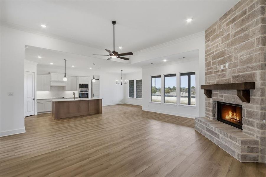 Dual tone kitchen with open floor plan, light countertops, a center island with sink, ceiling fan, and ornamental molding