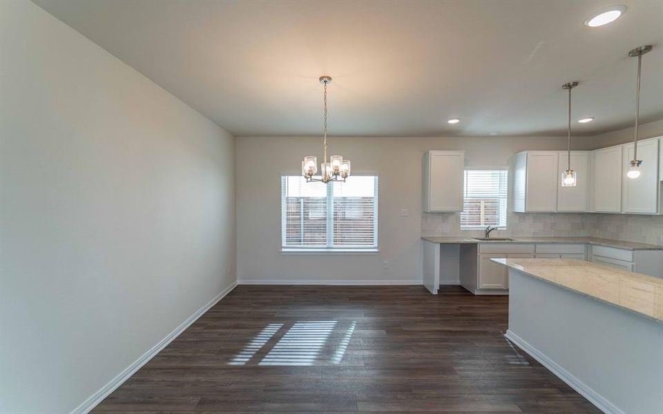 Open-concept living space featuring wood-finish flooring, a contemporary chandelier, and a bright window with blinds