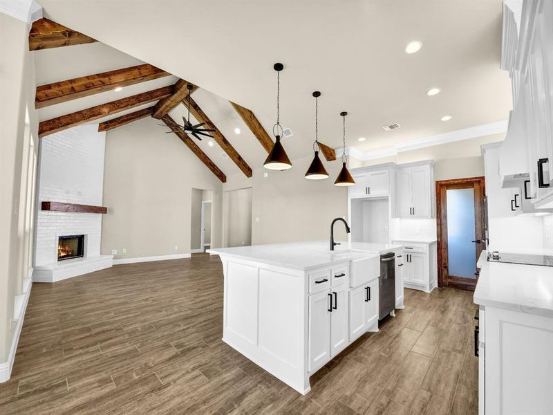 Kitchen with white cabinetry, a fireplace, ceiling fan, stainless steel dishwasher, and a kitchen island with sink