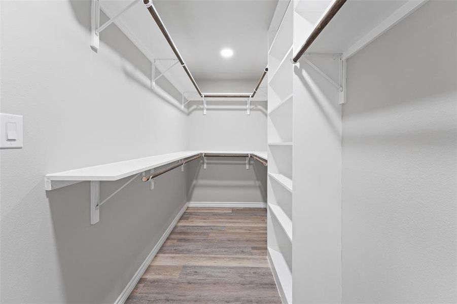 Spacious walk-in closet featuring wood-finish flooring, recessed lighting, white built-in shelving, and multiple hanging rods Spacious walk-in closet featuring wood-finish flooring, recessed lighting, white built-in shelving, and multiple hanging rods