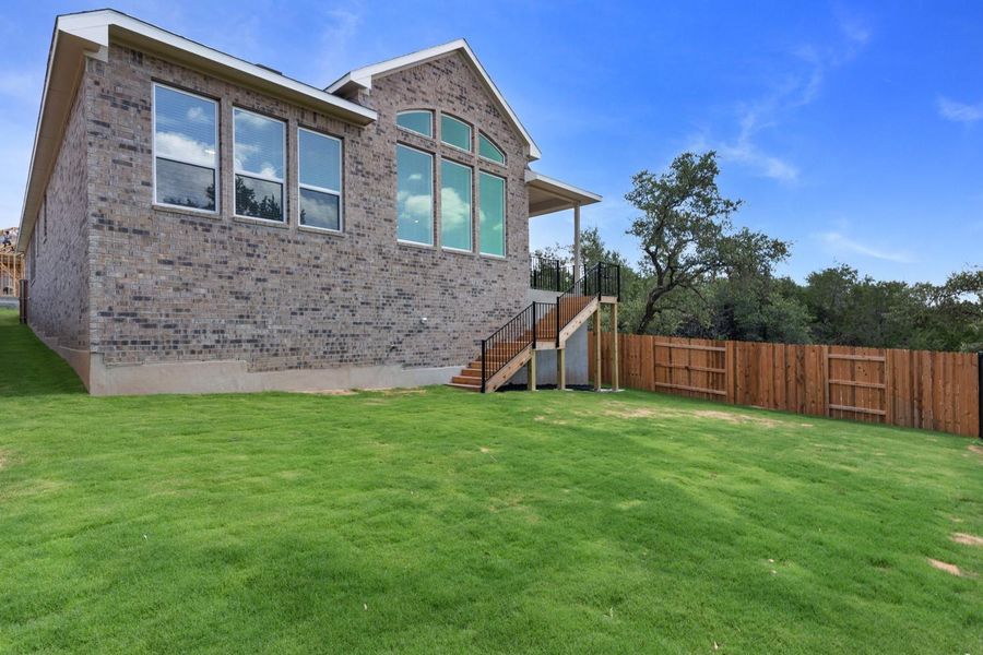 A spacious backyard with vibrant green grass, a privacy fence, and an inviting elevated deck with stairs leading down.