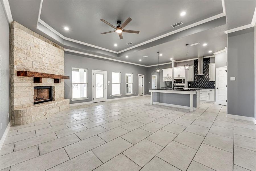 Kitchen with a tray ceiling, decorative light fixtures, a center island with sink, white cabinets, and a stone fireplace