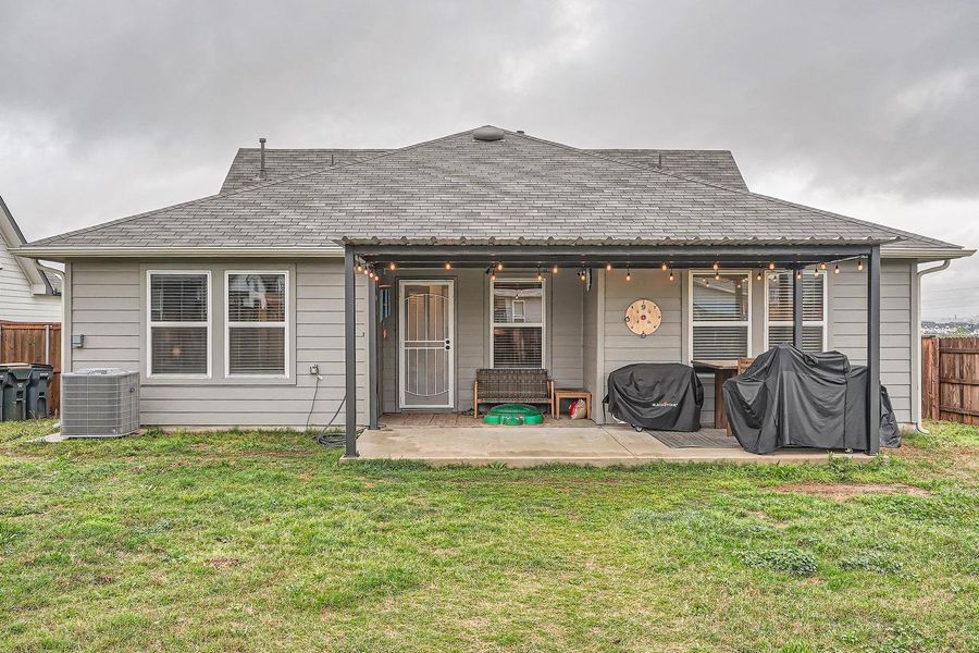 Rear view of house with a patio area, central AC, fence, and a lawn