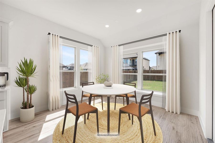 Bright dining area with round white table, four chairs, large windows, and light wood floors