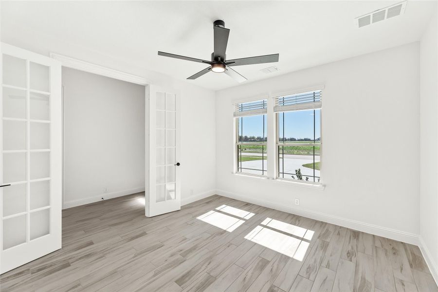 Empty room with light wood floors, ceiling fan, double windows, and French doors Empty room with light wood floors, ceiling fan, double windows, and French doors