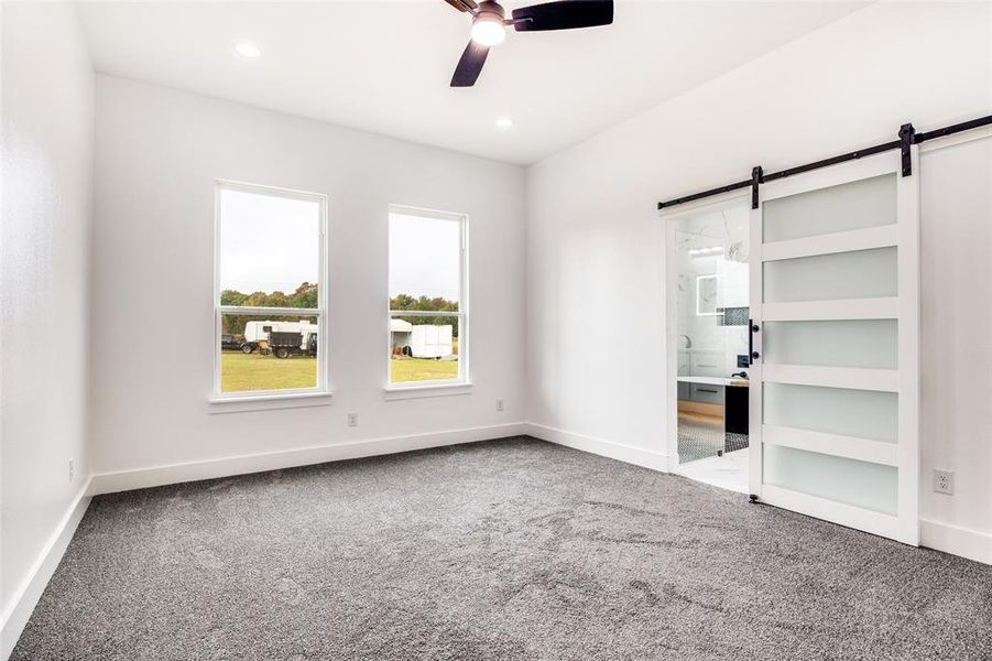 Unfurnished bedroom featuring a barn door, light carpet, ceiling fan, ensuite bathroom, and recessed lighting Unfurnished bedroom featuring a barn door, light carpet, ceiling fan, ensuite bathroom, and recessed lighting