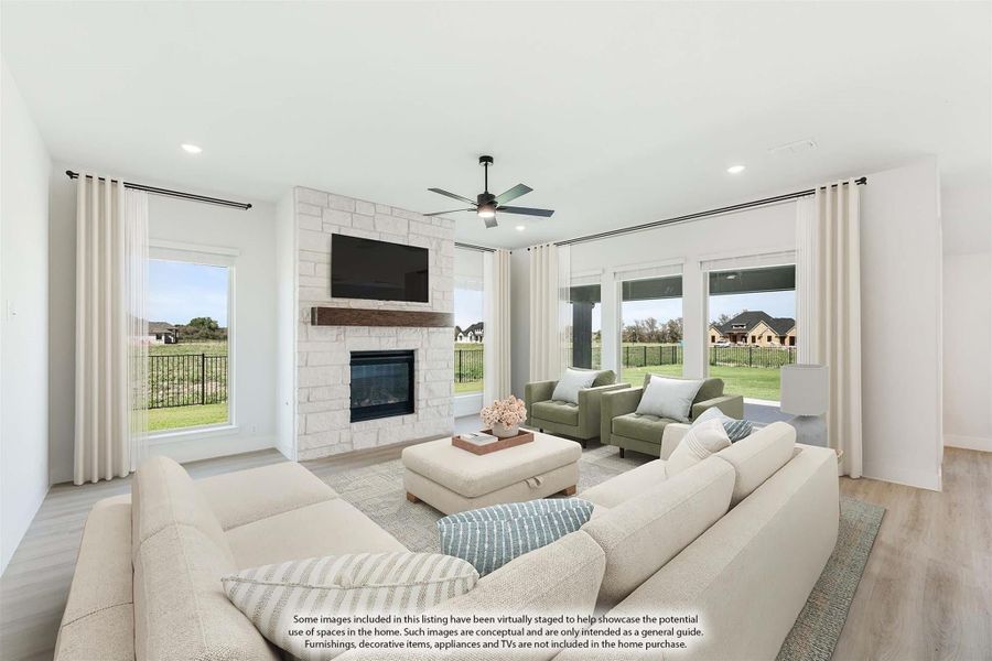 Bright living room with stone fireplace, ceiling fan, large windows, and hardwood floors