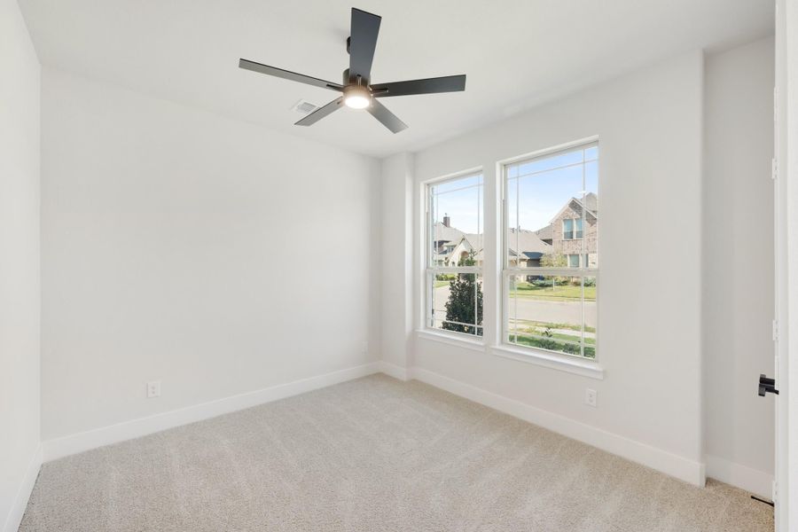Empty bedroom with carpet flooring, black ceiling fan, and two windows overlooking a neighborhood street Empty bedroom with carpet flooring, black ceiling fan, and two windows overlooking a neighborhood street
